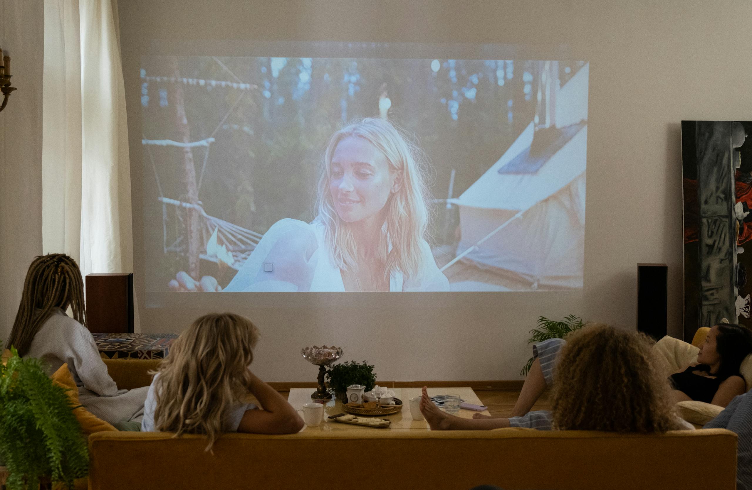 Group of women enjoying a movie night at home, projected on a screen in a cozy living room.