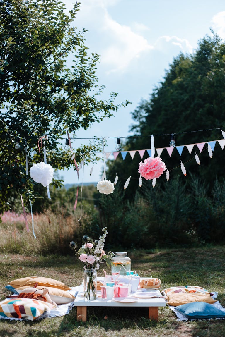 Outdoor picnic setup with vibrant decor, bunting, and cushions under a sunny sky.