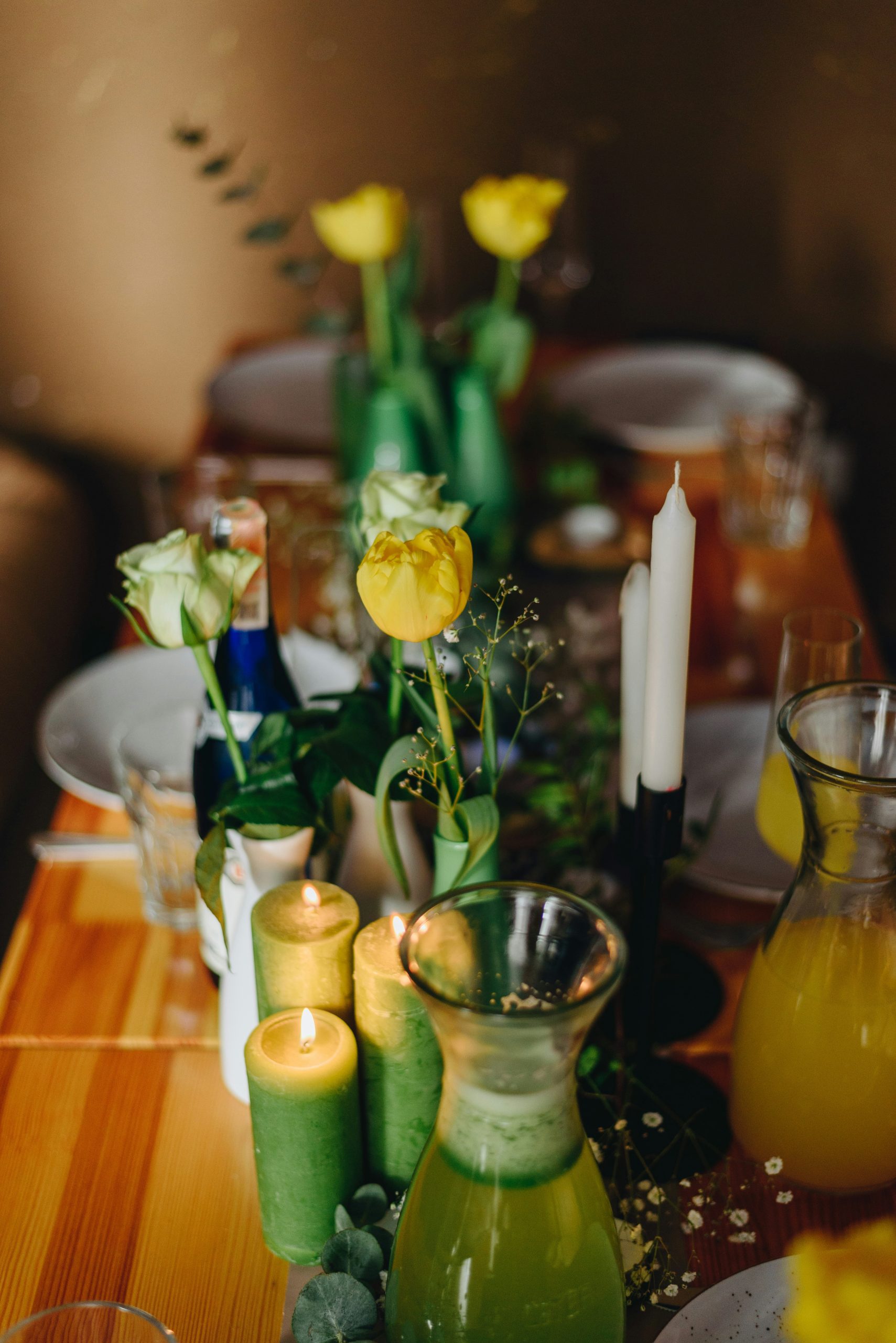 A beautifully set dining table with various spring comfort food dishes, fresh flowers in a simple vase, lit candles, cloth napkins and rustic tableware,