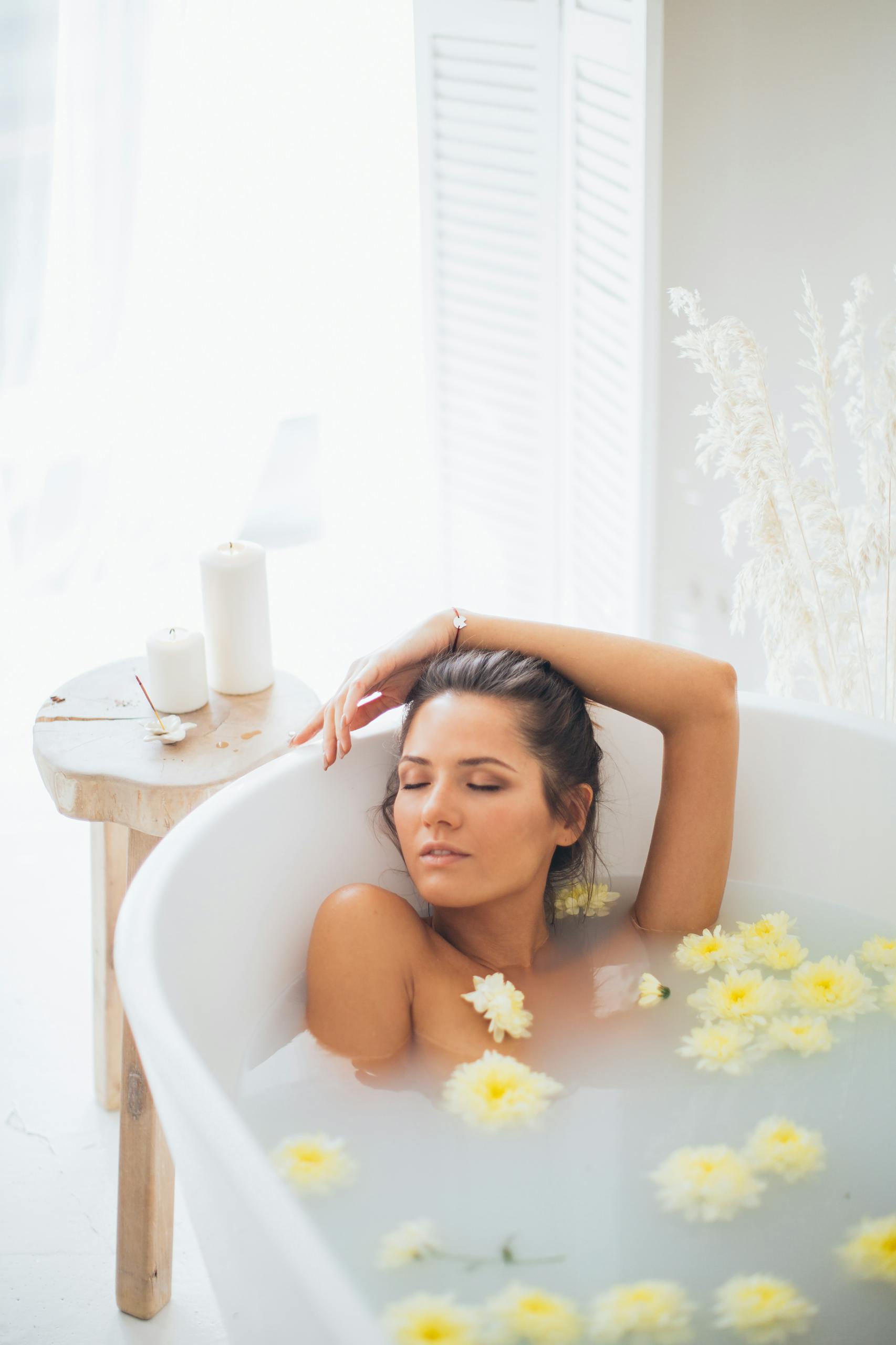 Woman enjoying a soothing bath with yellow flowers and candles, embracing relaxation.