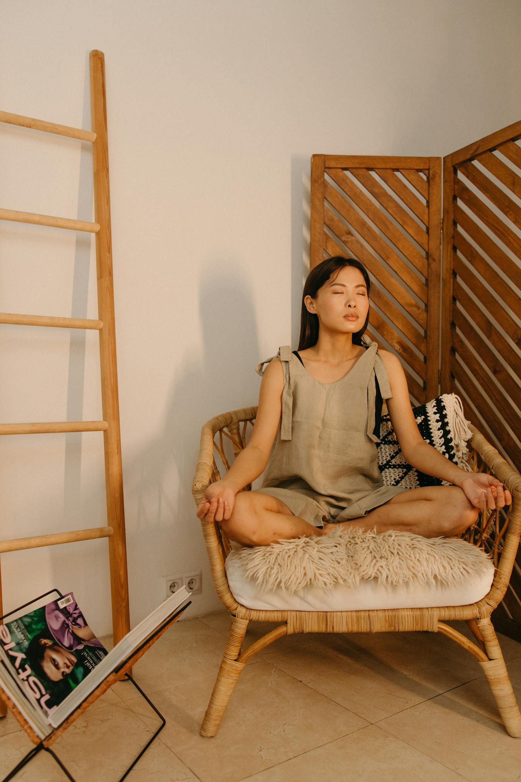 A serene Asian woman sits meditating in sukhasana pose indoors behind a room divider