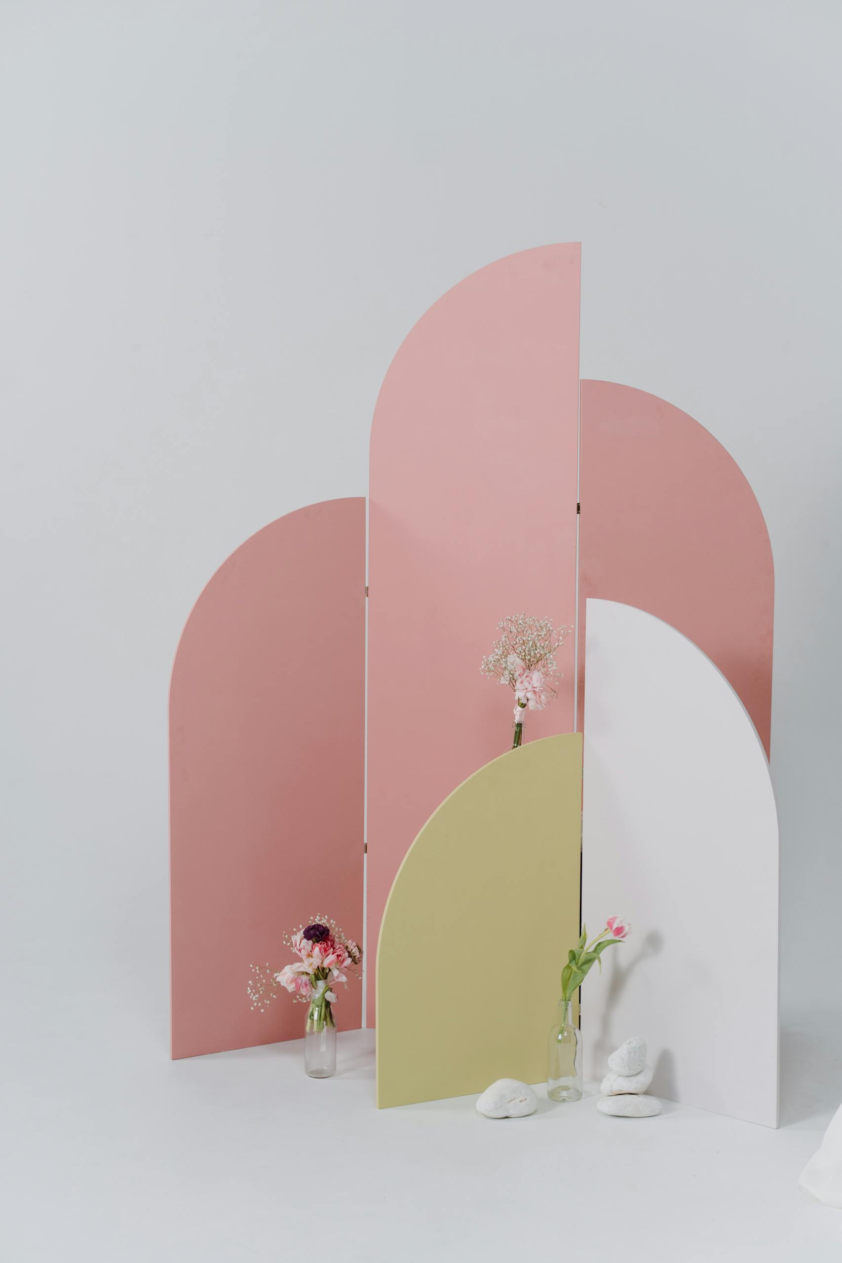 Minimalist composition featuring flowers in vases against a pastel-colored room divider.