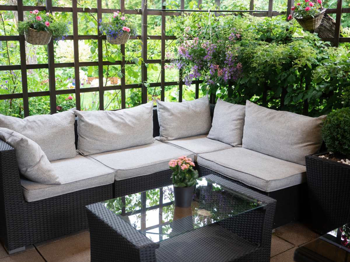 A Black rattan garden corner sofa  with crem cushions and a black rattan glass topped table 