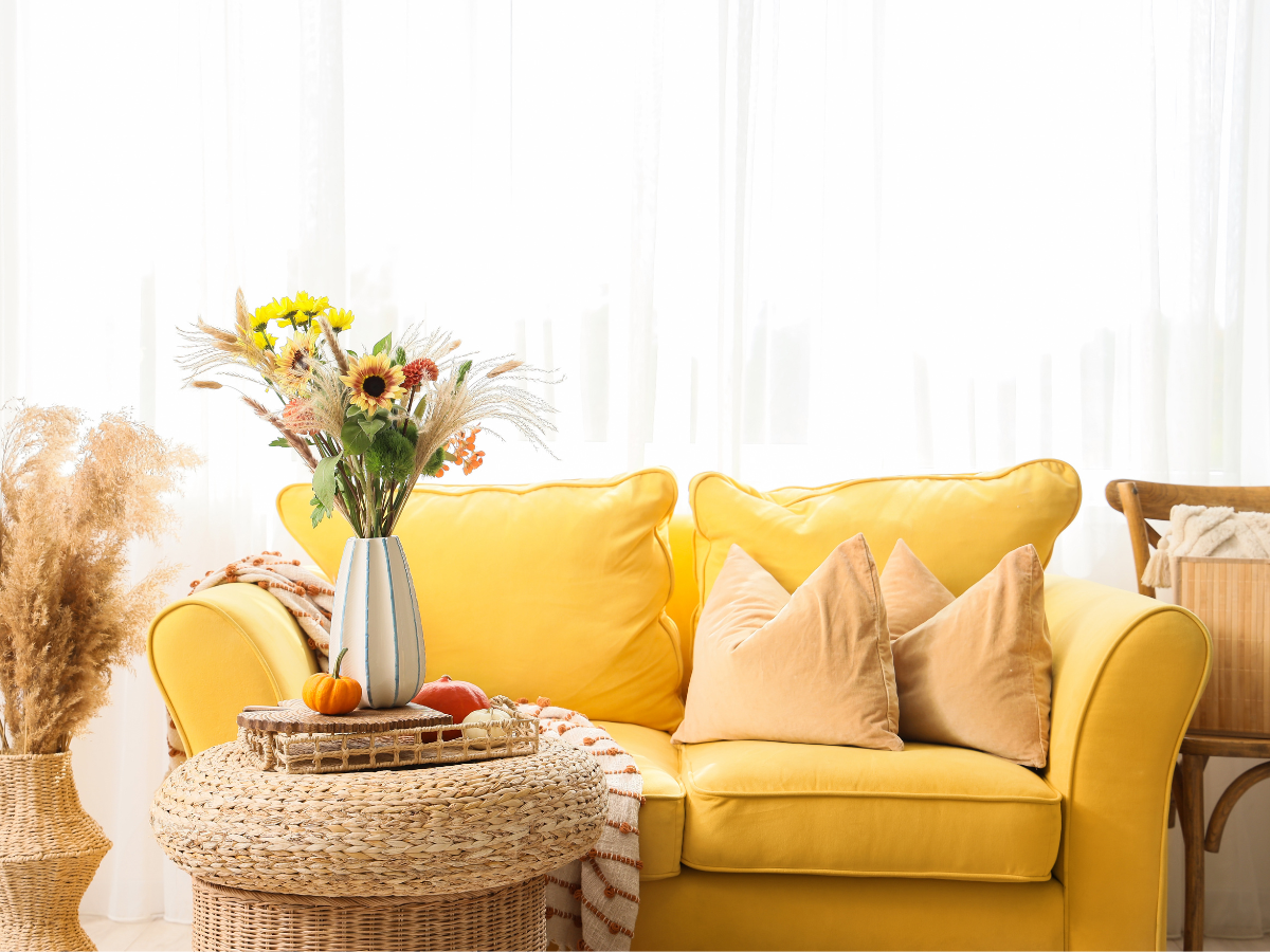 A styled corner of a living room — a light yellow sofa fresh flowers in a simple vase, Feels like a boutique B&B rather than someone's front room.