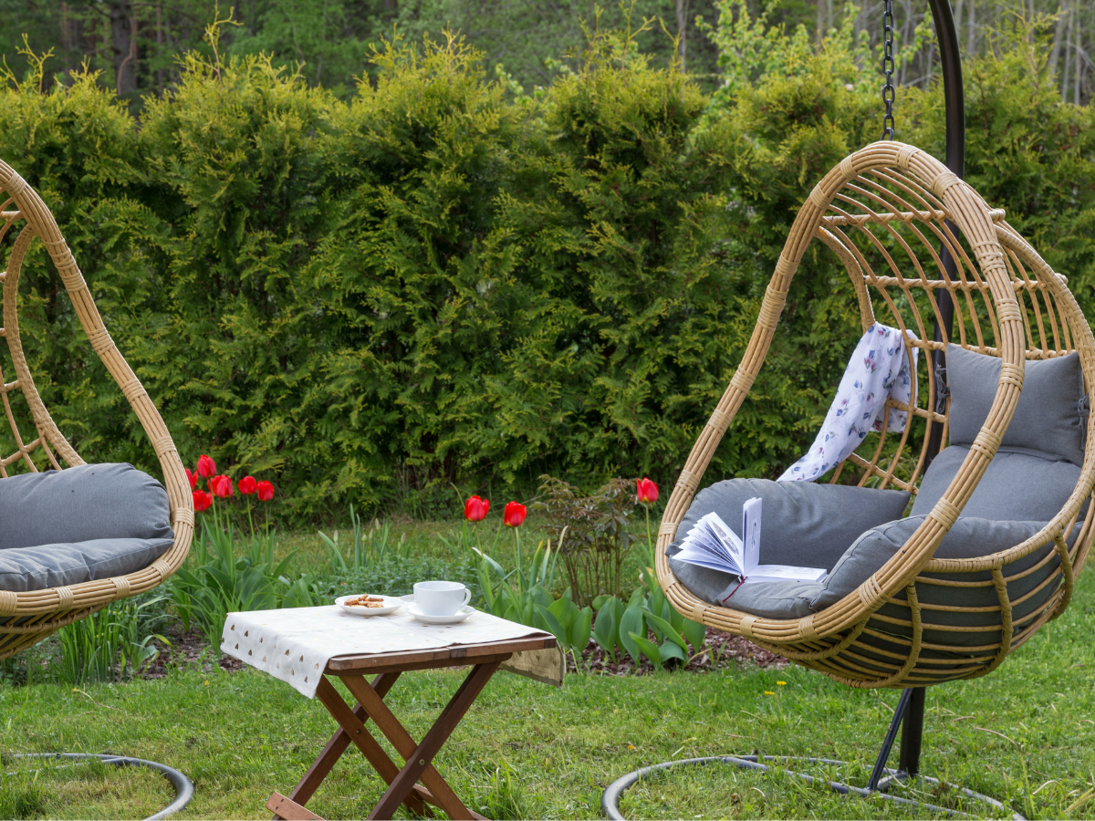A Pair of Swinging Rattan Egg Chairs on green sunny garden lawn with a small table and white table cloth
