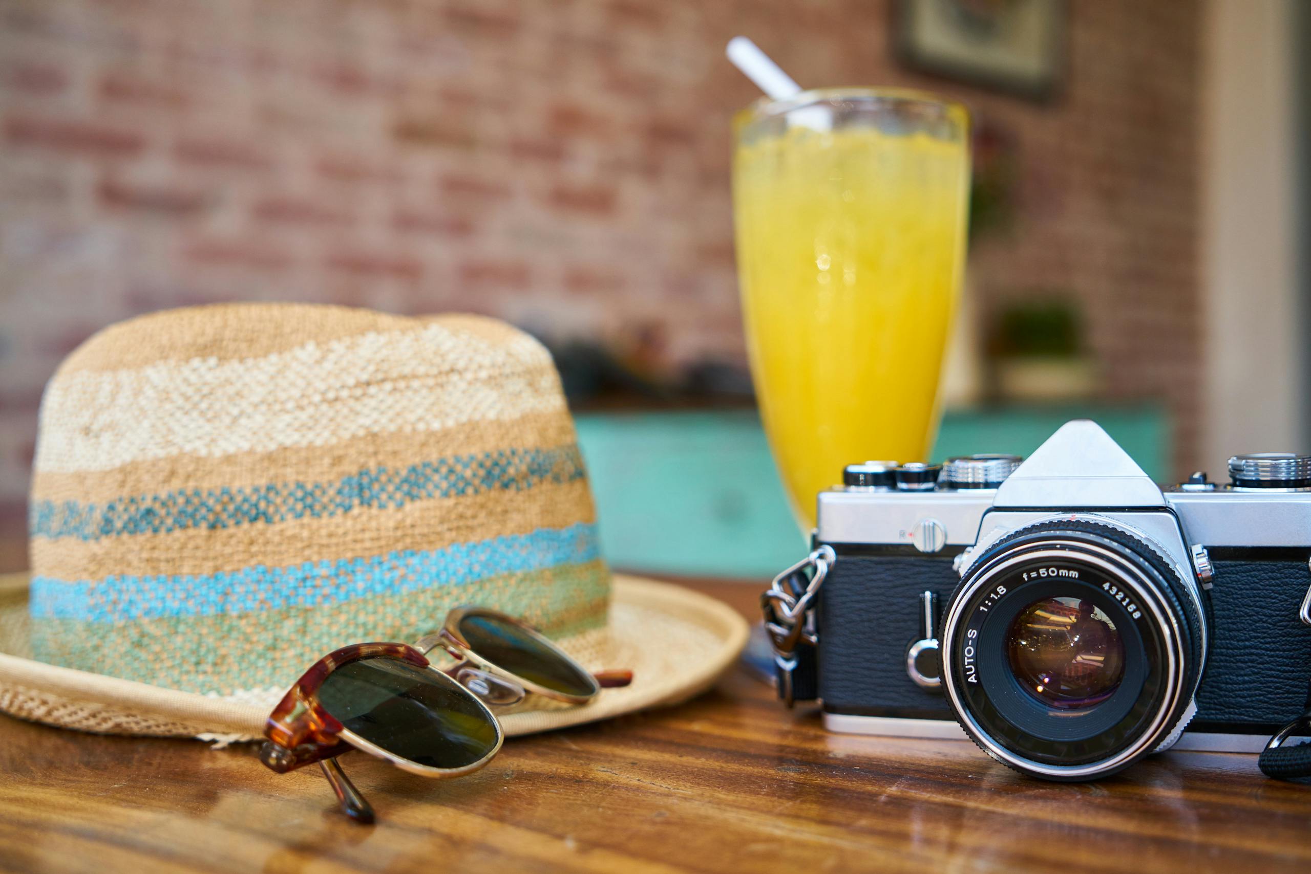 A stylish scene showcasing a vintage camera, hat, and orange juice, evoking summer staycation bucket list vibes.