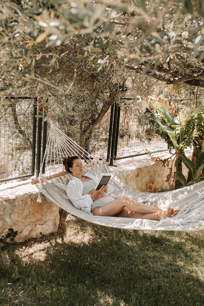 A woman enjoys a peaceful afternoon reading in a hammock surrounded by lush greenery.