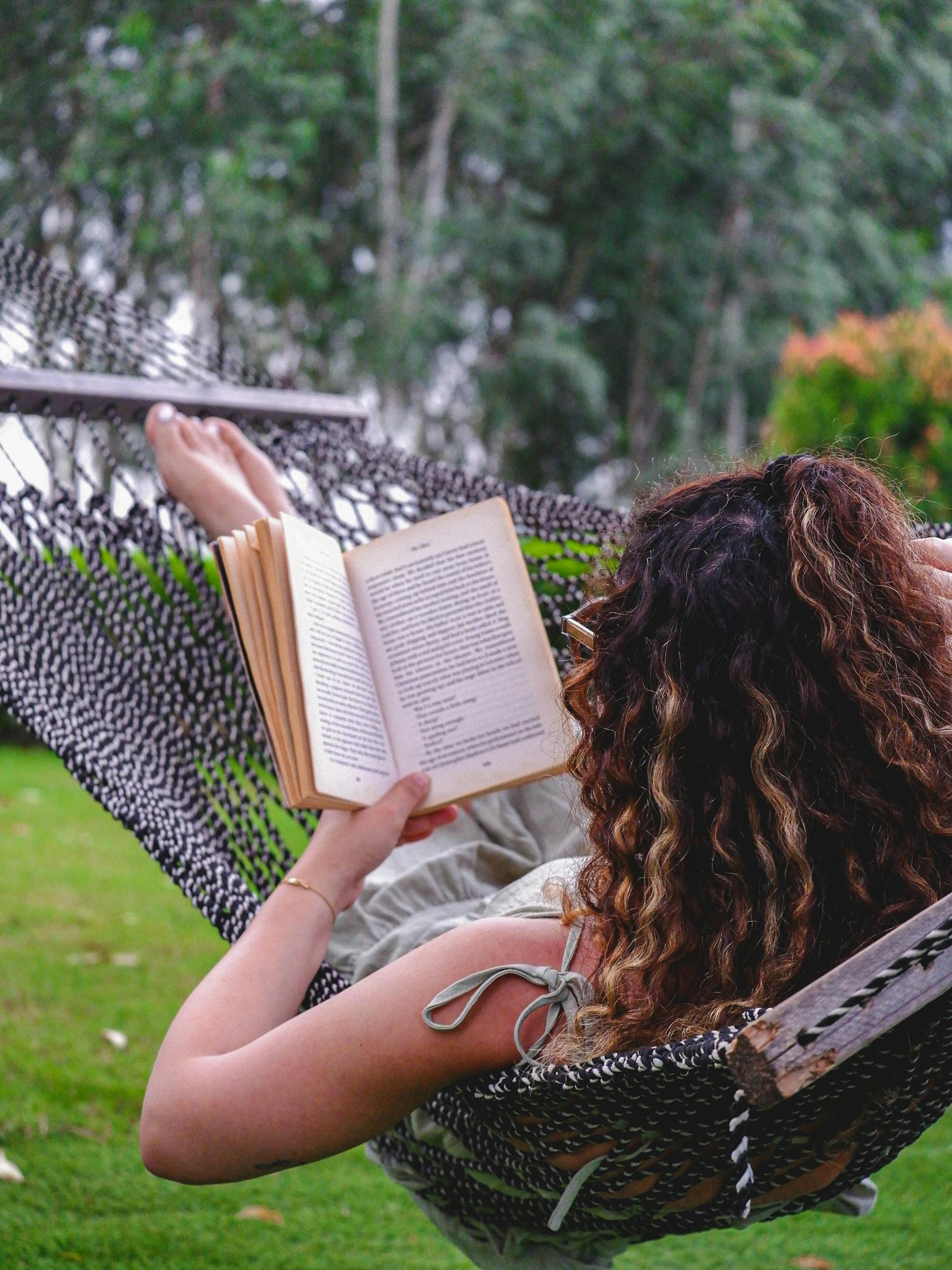 A woman enjoys a peaceful moment reading a book in a hammock outdoors.