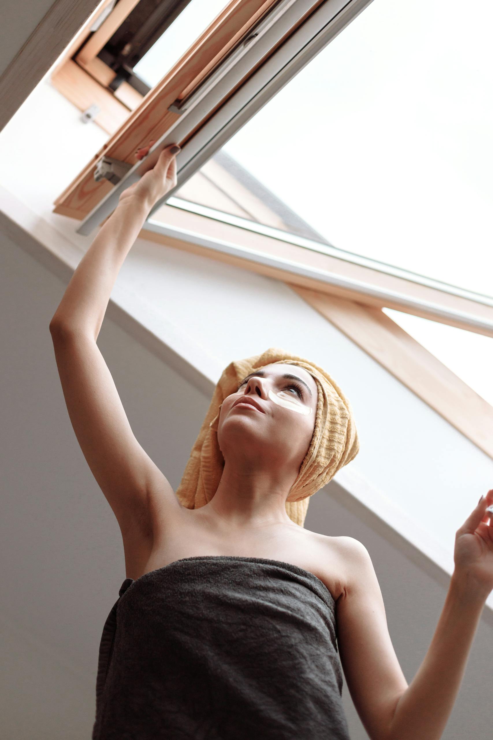 A woman in a towel adjusts a skylight, embracing natural light in a modern bathroom. Morning House burping routine