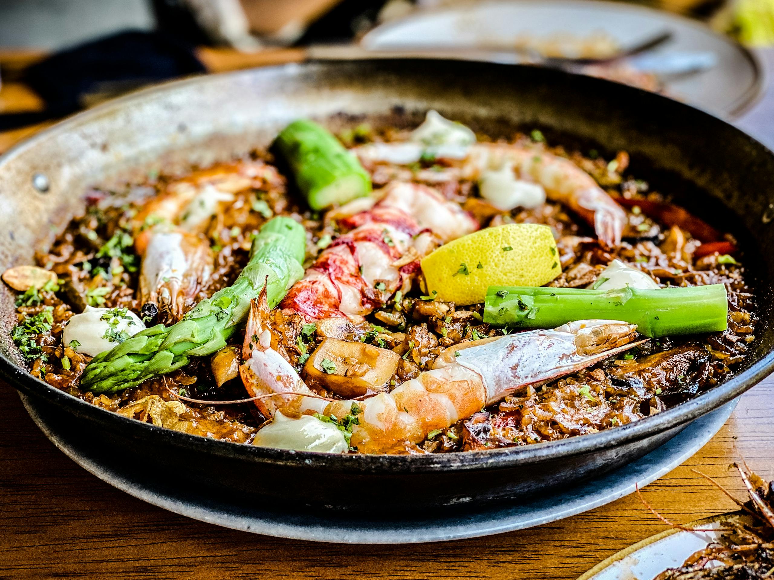 Close-up of delicious seafood paella with shrimp, asparagus, and lemon in a rustic pan.