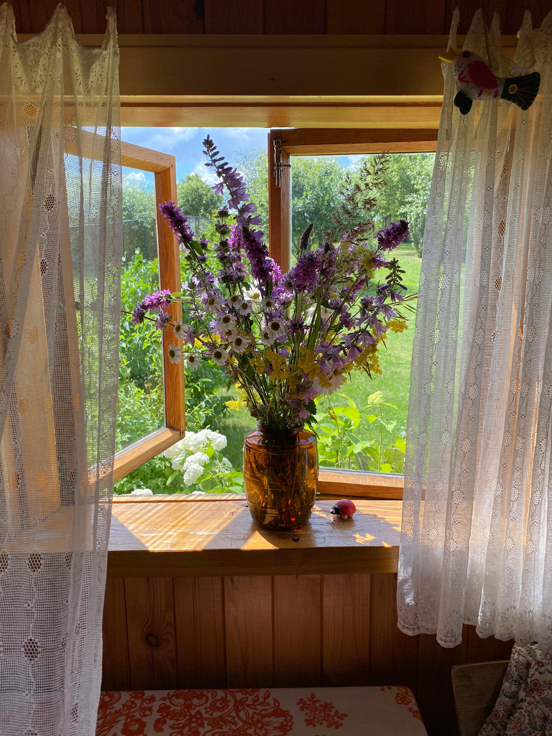 Colorful wildflowers in a vase by an open window, inviting warmth and summer vibes into the room.