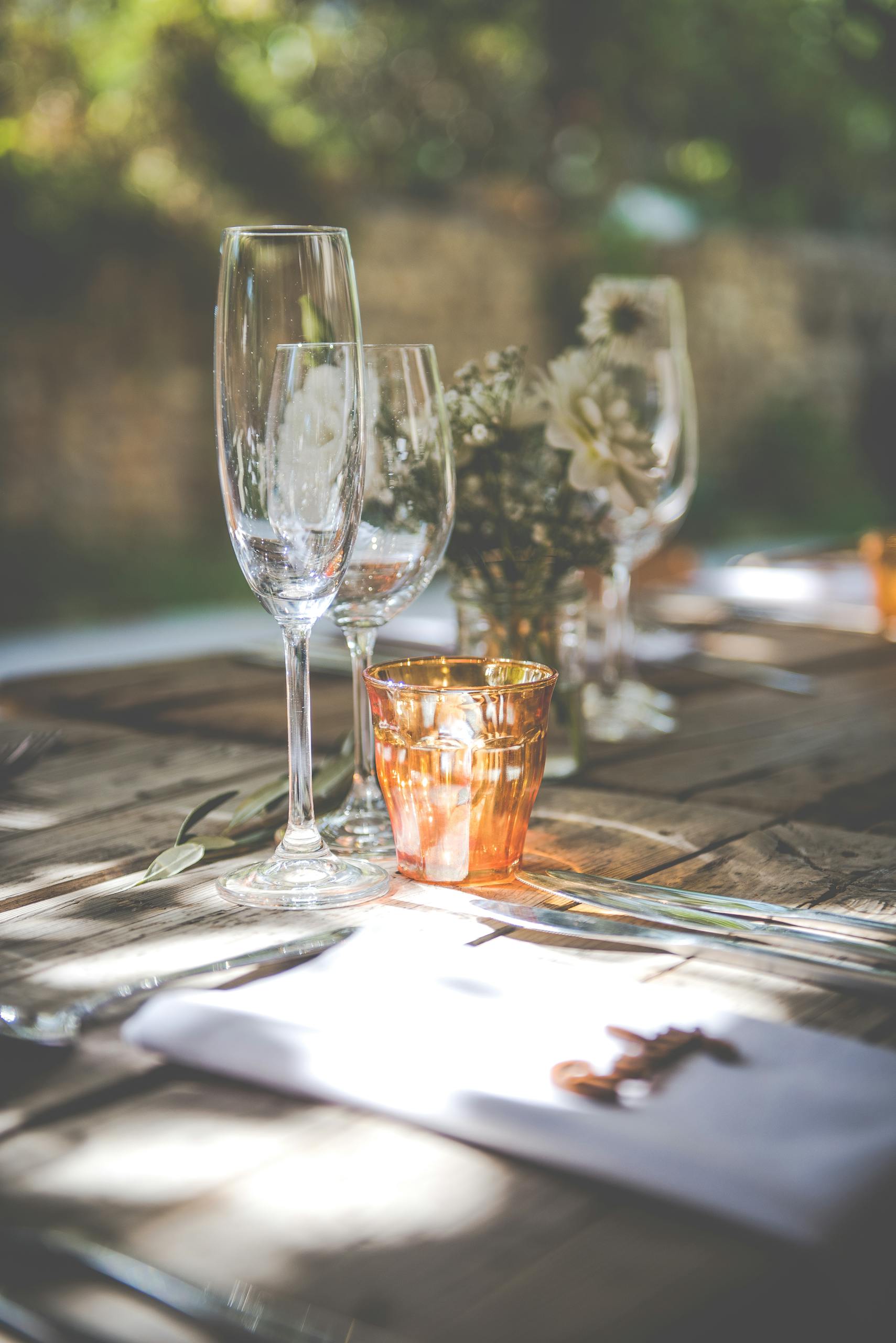 Elegant outdoor table setting with glassware and flowers in natural sunlight.