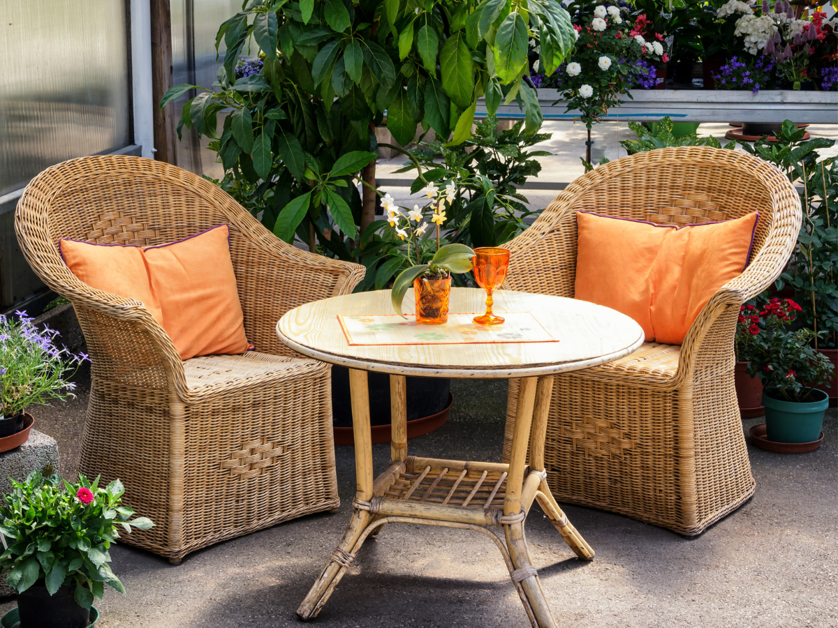 outdoor rattan bistro set with Orange cushions and candles and summer plants on a patio — holiday home feel outdoors