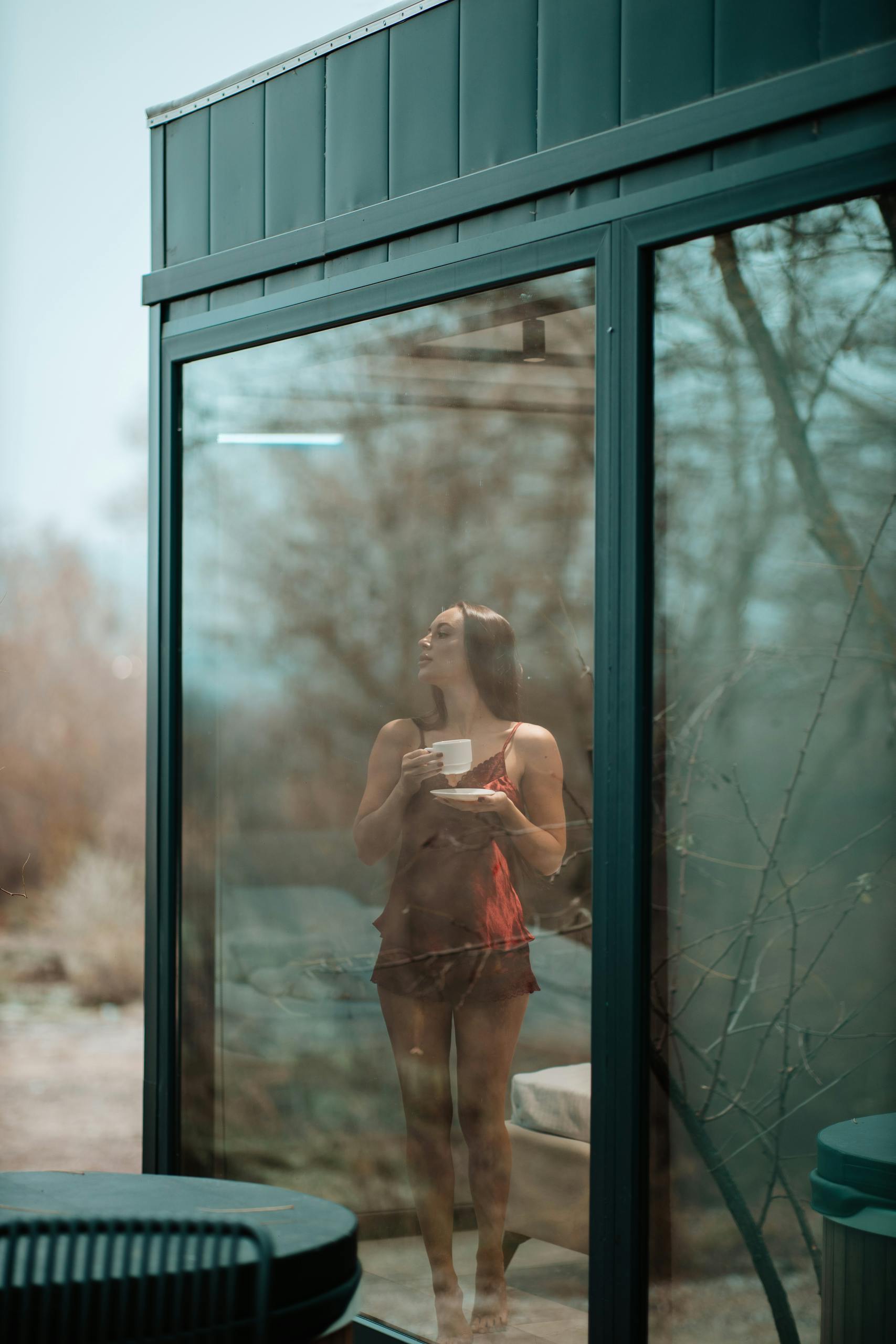 Woman enjoys a tranquil morning with coffee, reflected through a large window.