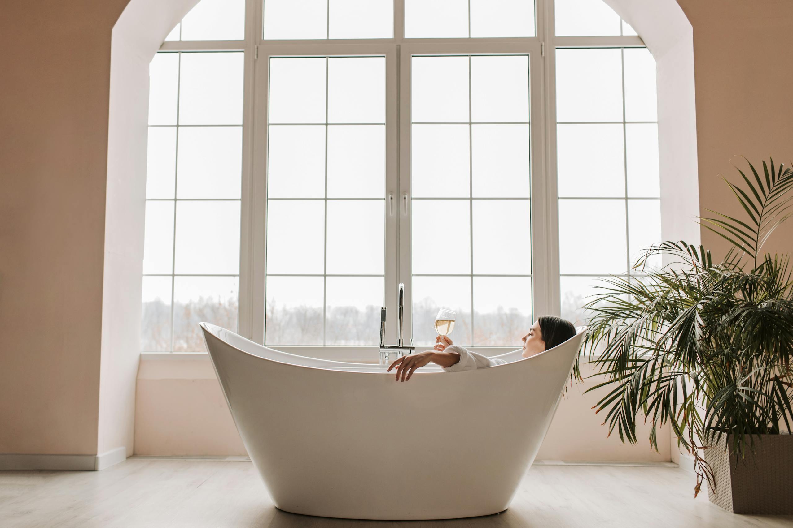 A serene scene of a woman enjoying a glass of wine while relaxing in a modern bathtub indoors.