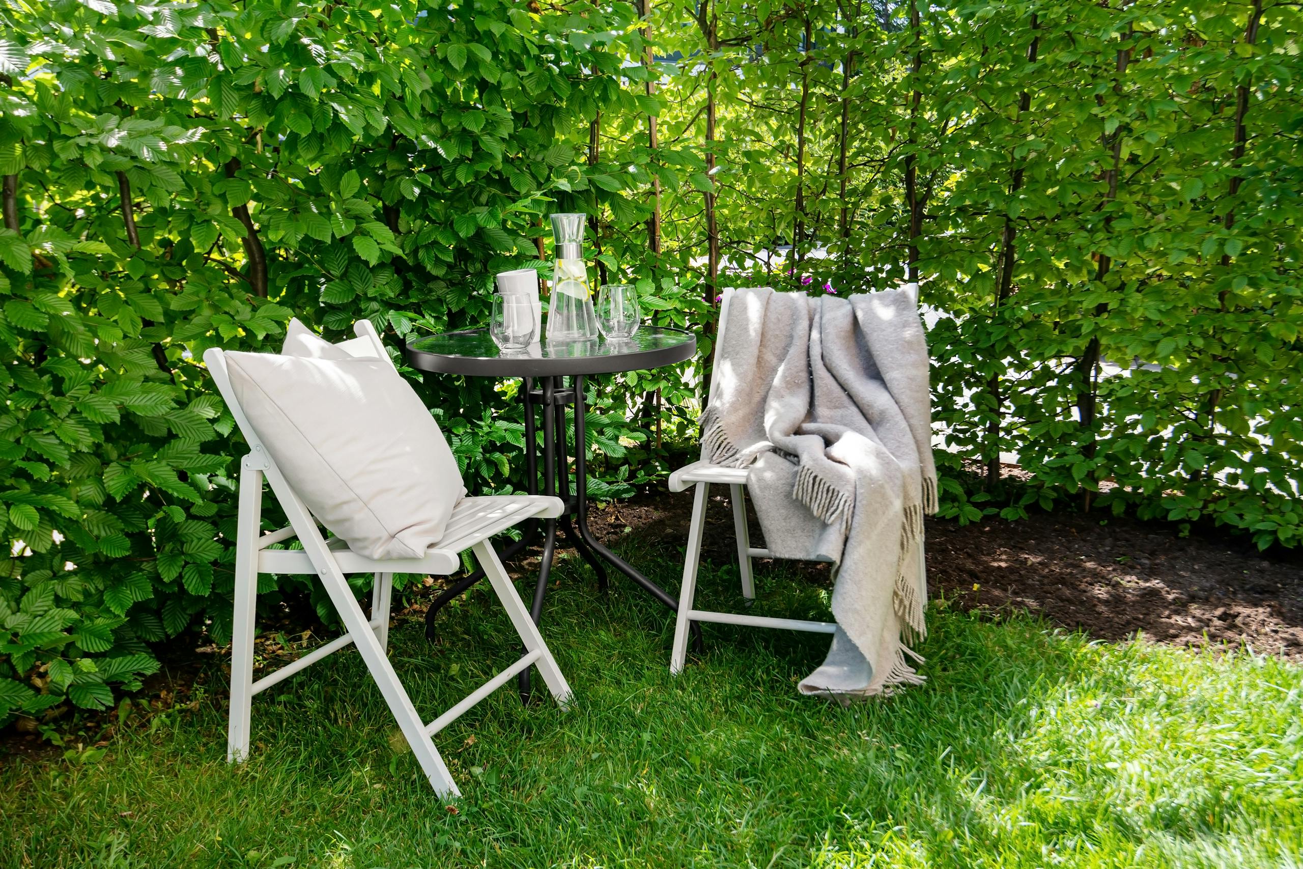 Relaxing outdoor patio setup with chairs, table, and green garden backdrop.