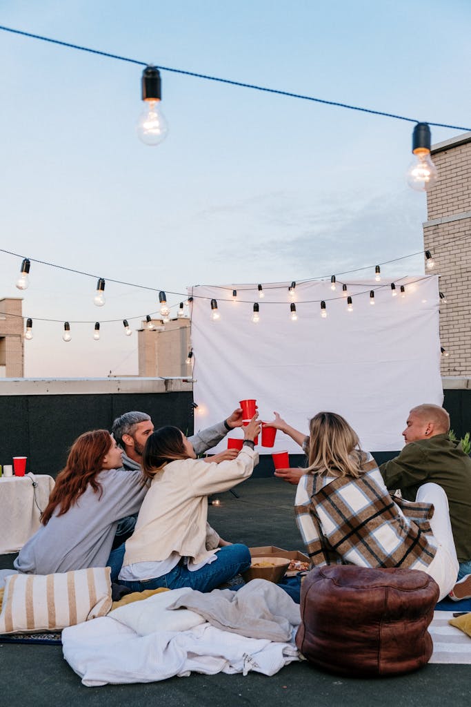 A group of friends enjoying an outdoor garden cinema setup at home on a summer night with projector and string lights for summer staycation night in