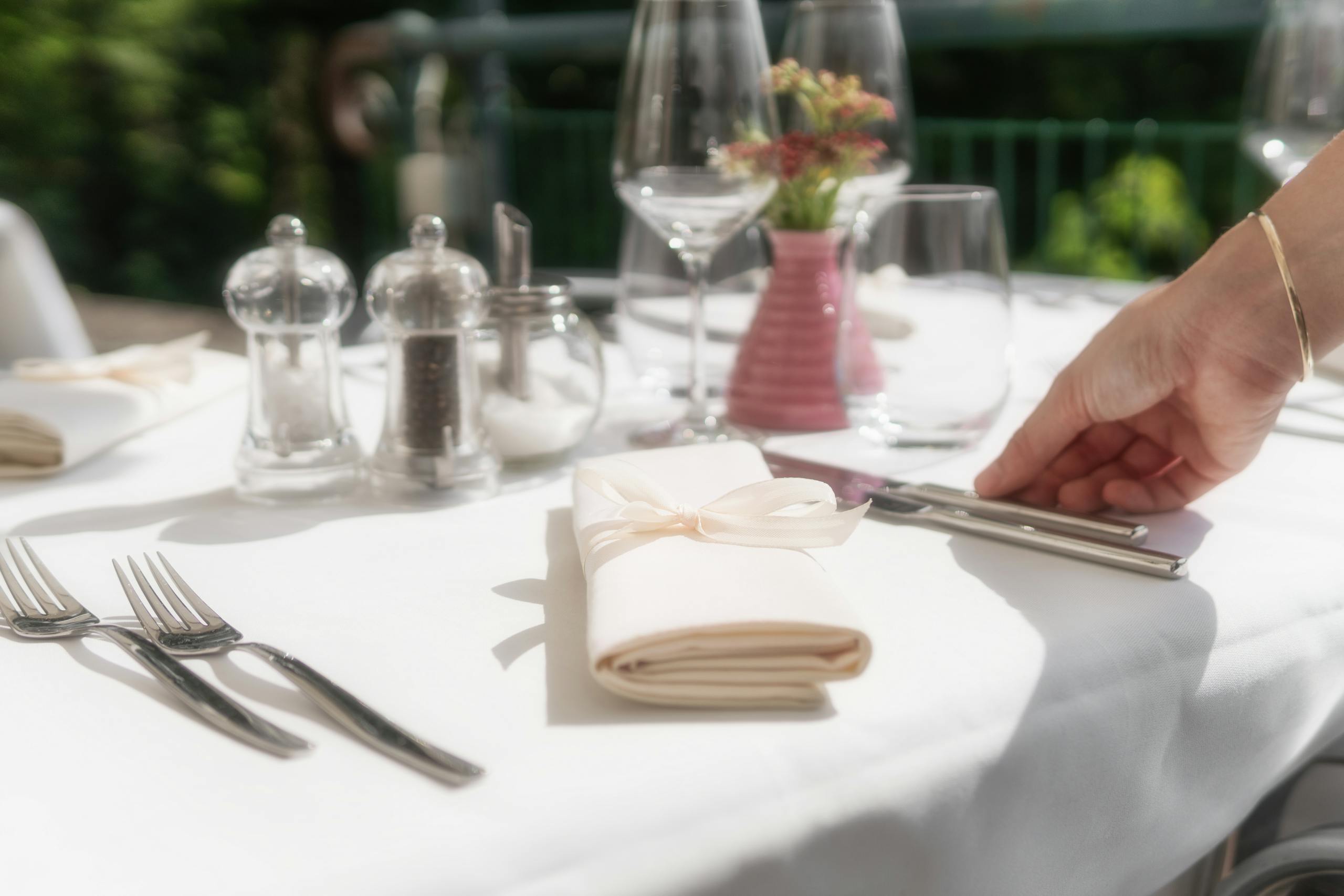 A luxurious table setting featuring a white napkin with a ribbon, fine glassware, and silverware in a garden