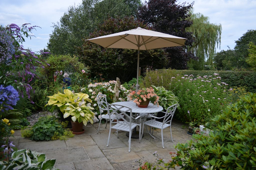 A serene bistro style garden patio featuring a table with chairs, umbrella, and vibrant flowers in full bloom for a backyard Garden staycation