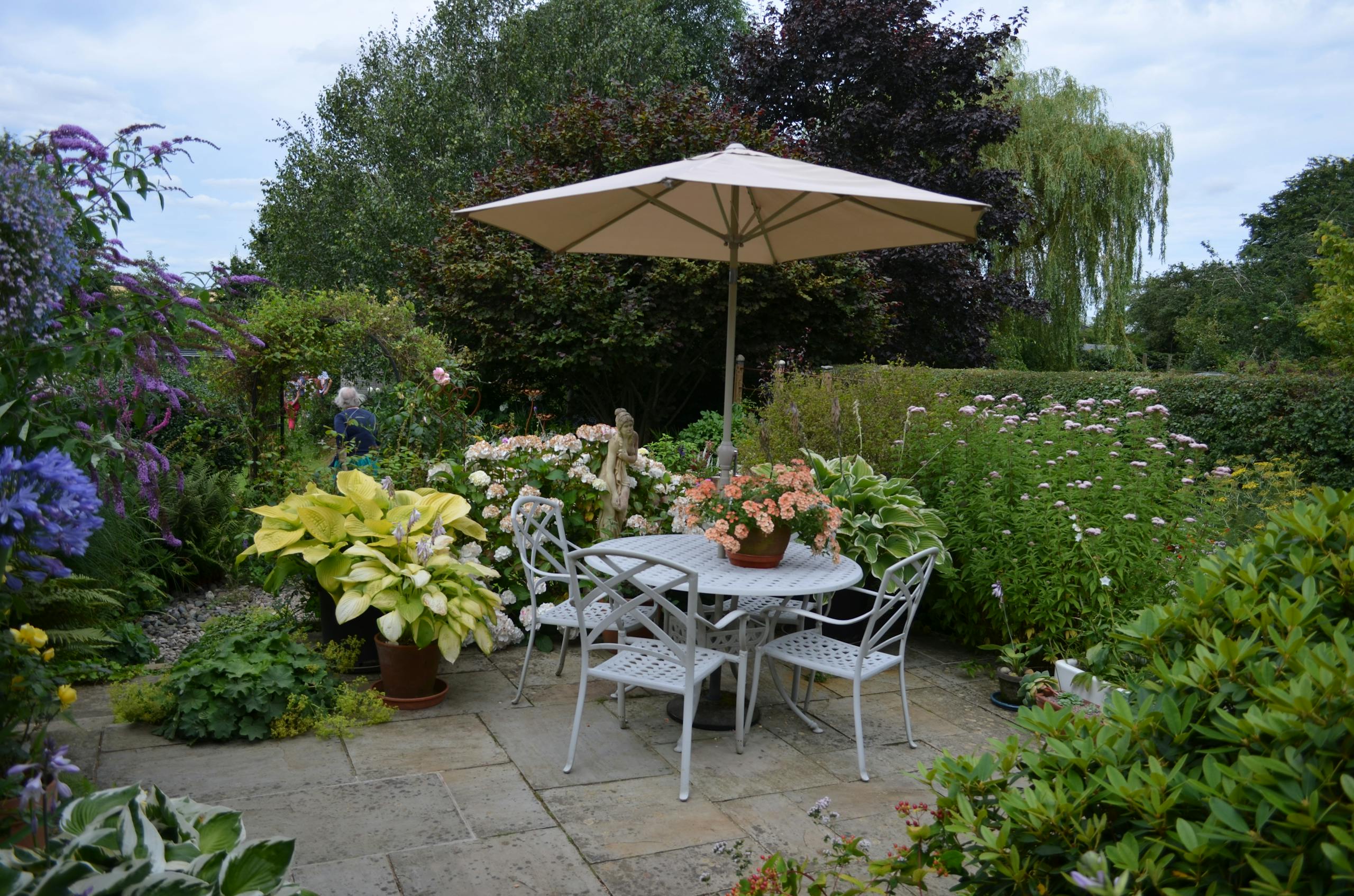 A serene bistro style garden patio featuring a table with chairs, umbrella, and vibrant flowers in full bloom.