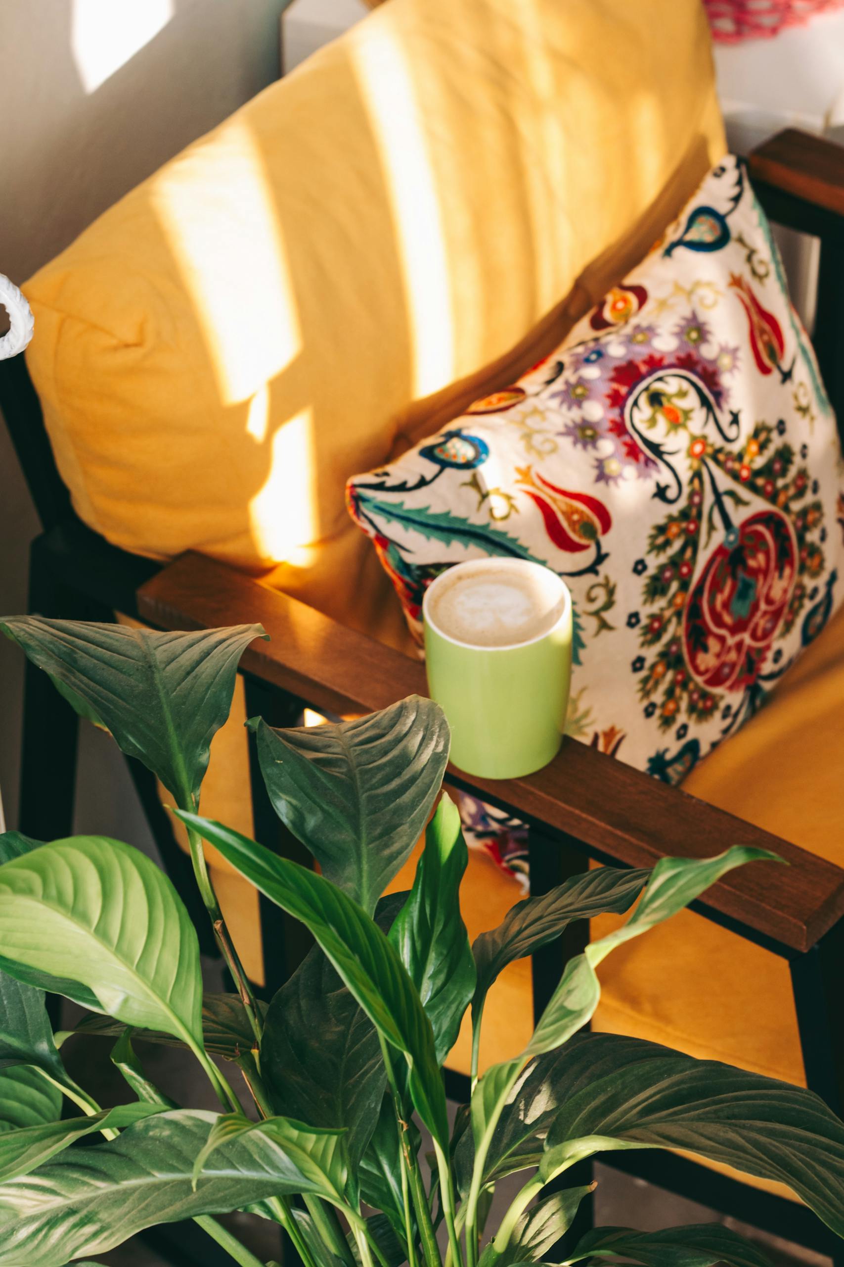 A vibrant indoor setup with a yellow cushion, patterned pillow, coffee mug, and lush plants.