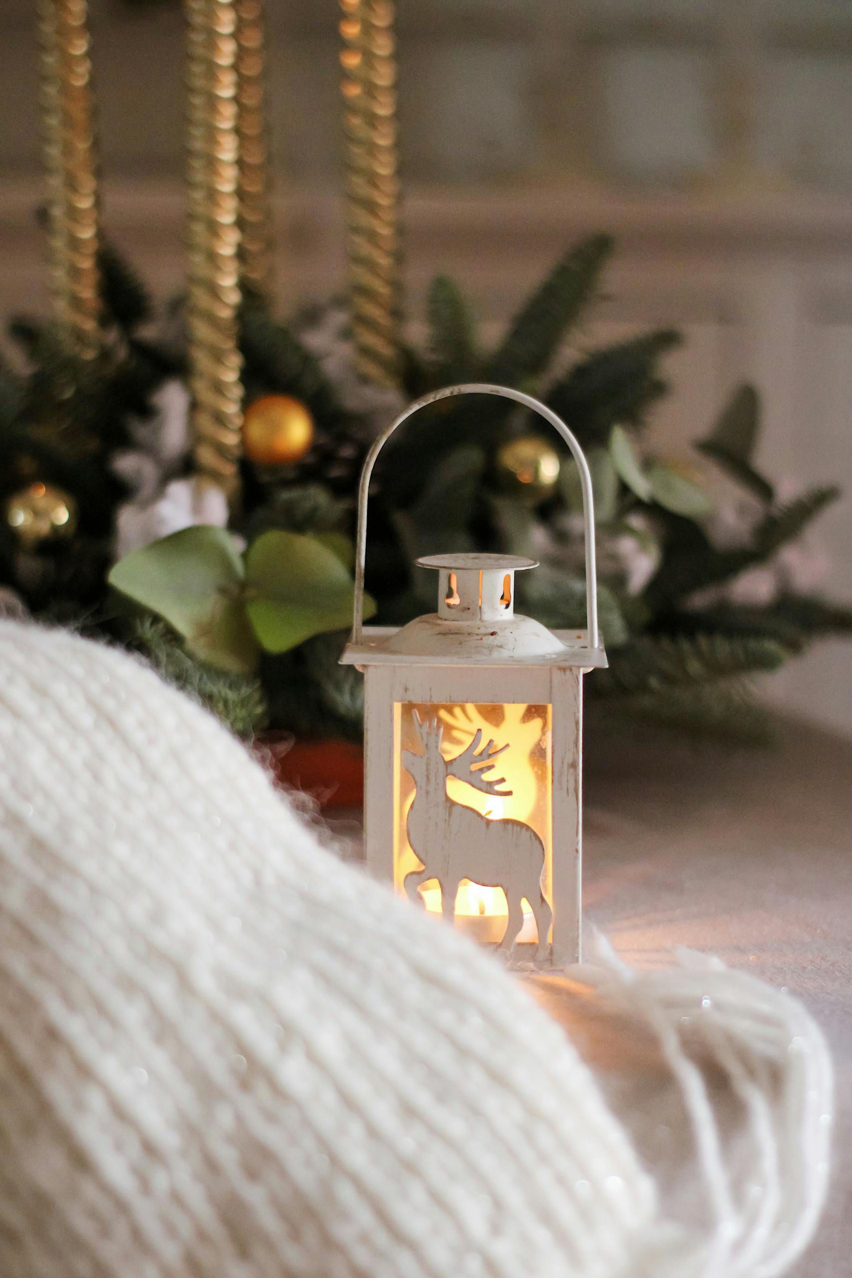 A warm holiday scene featuring a candlelit lantern with Christmas decor and a white knitted sweater.