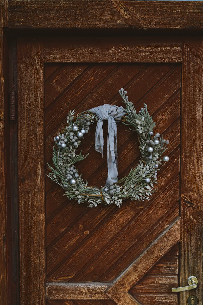 Elegant rustic Christmas wreath with silver ornaments on a wooden door, perfect for festive decoration.
