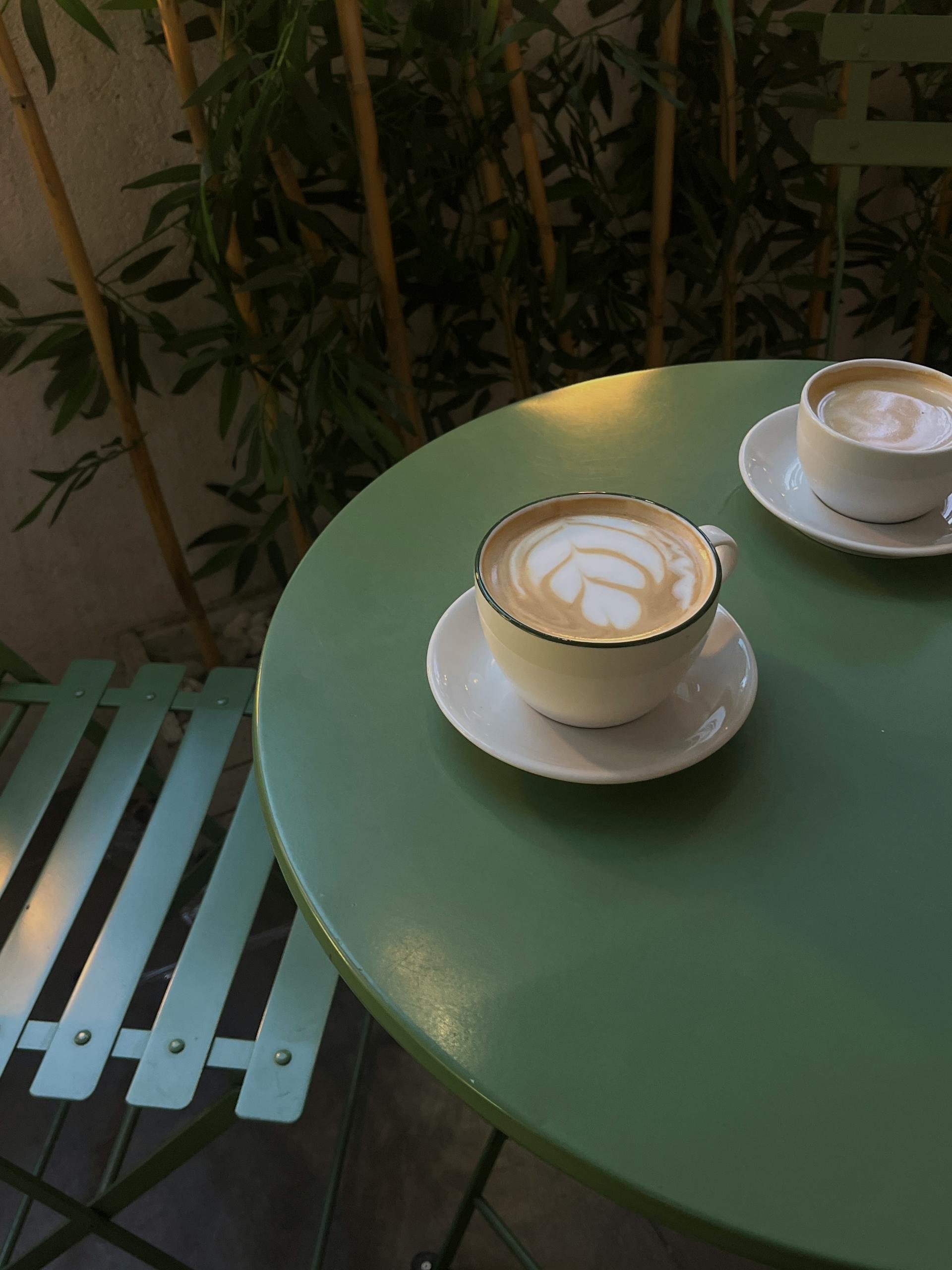 Green cafe table with two cappuccinos outdoors, perfect cozy setup.