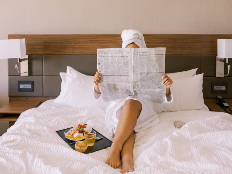 Woman reading newspaper in spa robe and towel enjoying hotel style breakfast in bed slow summer morning routine at home