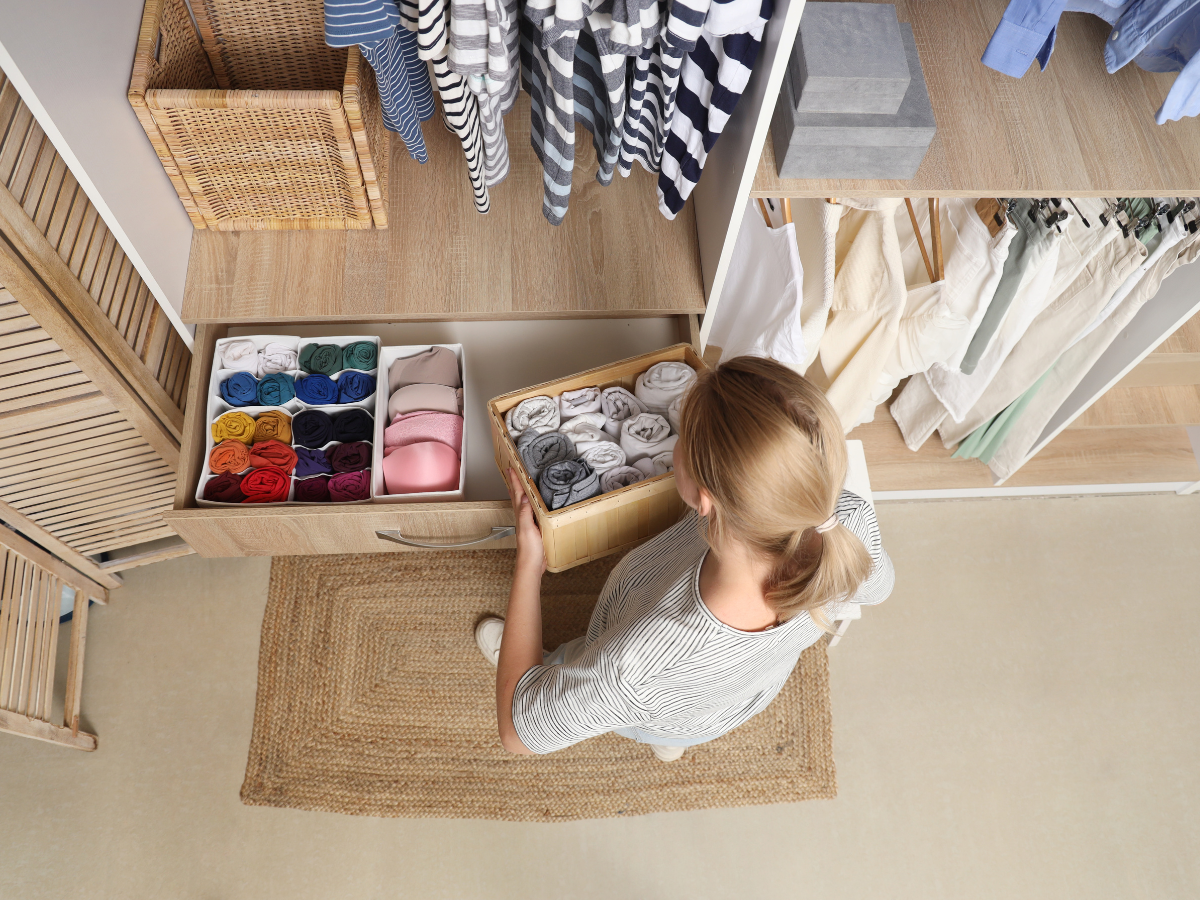 Woman sorting out wardrobe. Organised bedroom drawer with bamboo dividers and neatly folded clothes – bedroom organisation ideas on a budget