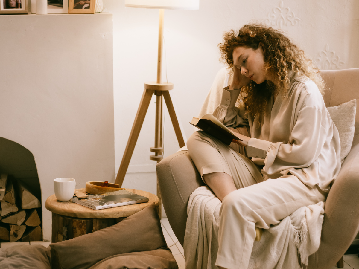 woman sat in an armchair in a cosy reading nook corner and lamp in home interior 