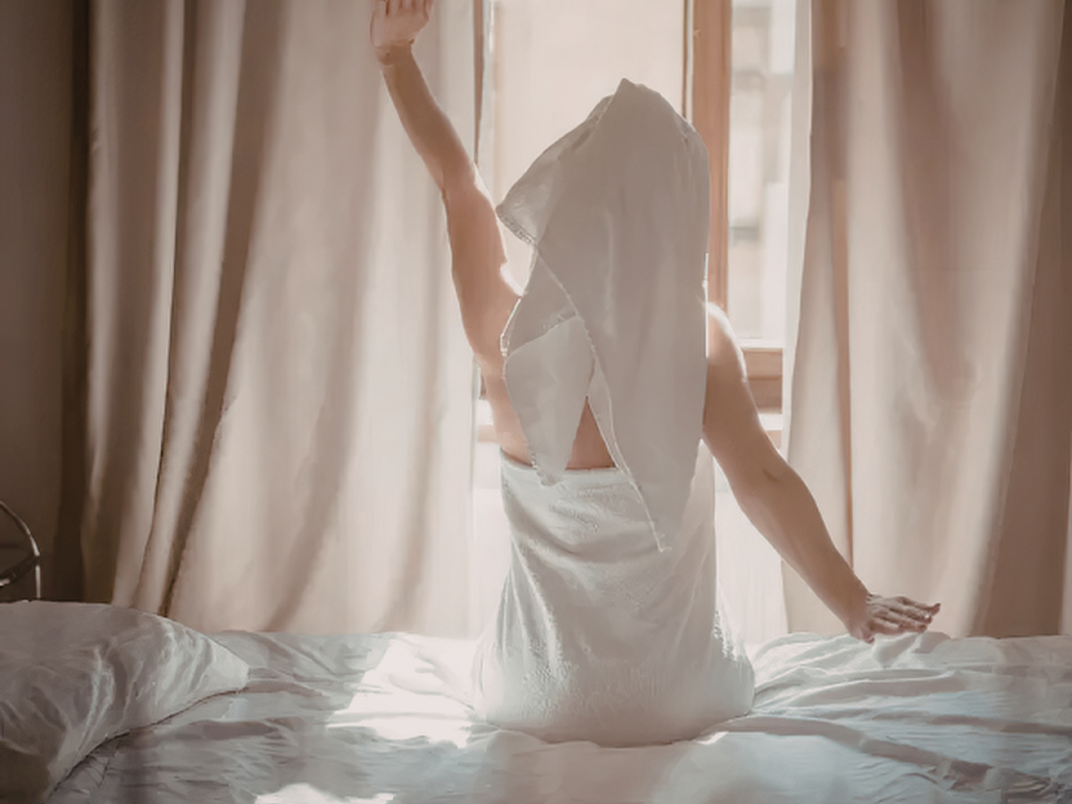 a woman opening a pair of blackout curtains in a cosy white bedroom