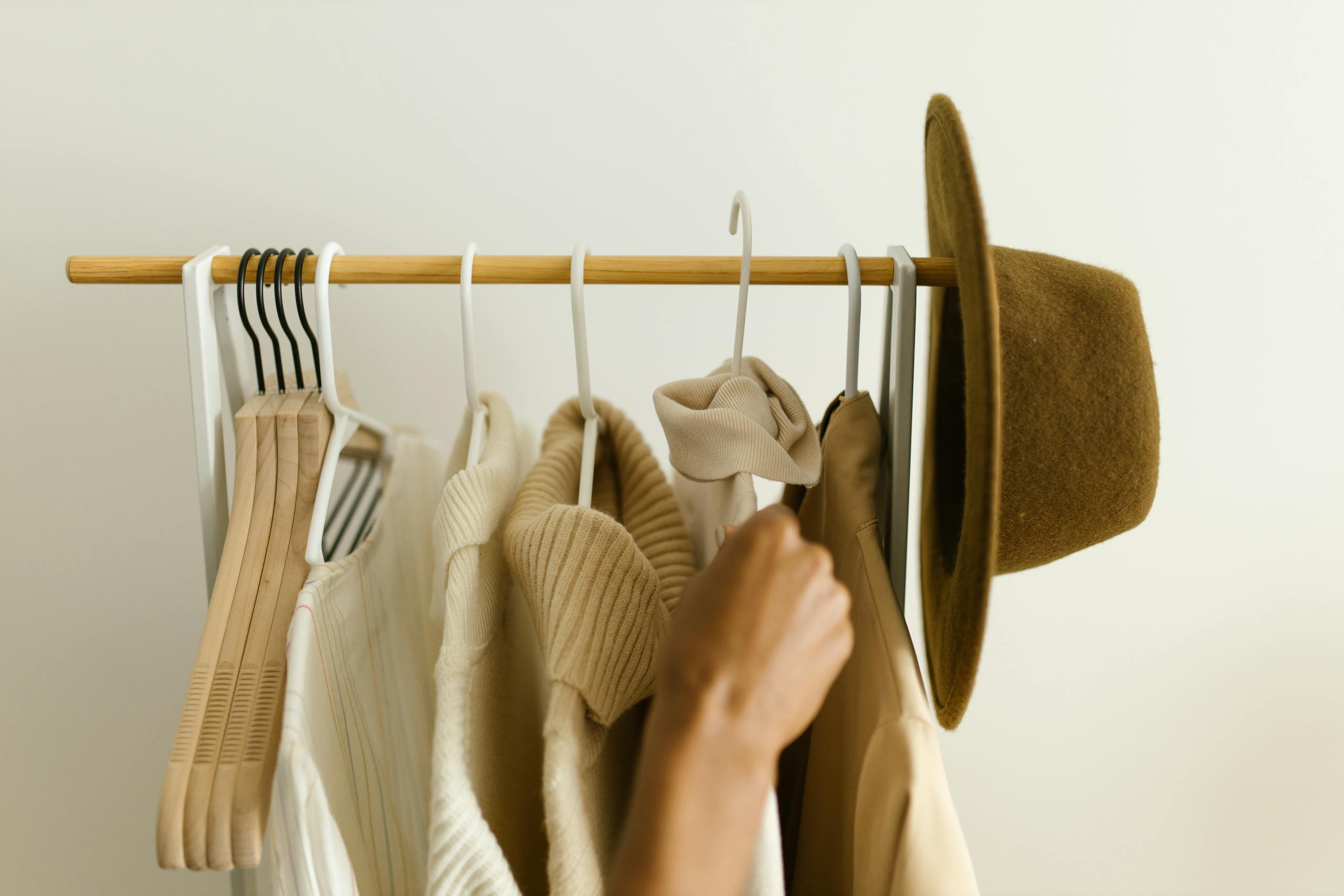 Organized Stylish beige and brown clothes on a rack with a hand reaching in.