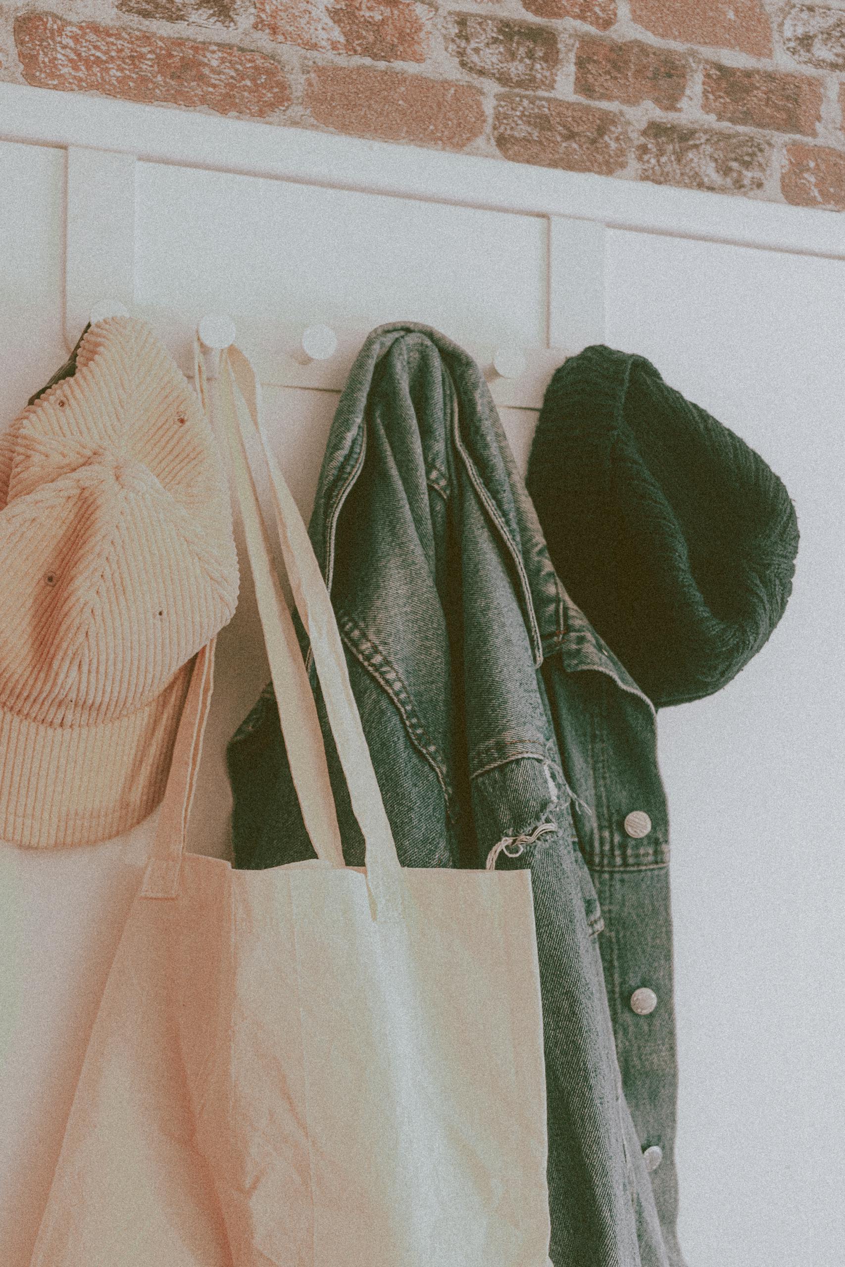 Warm hat with denim coat and light pink bag on round hanger on white wall in daylight