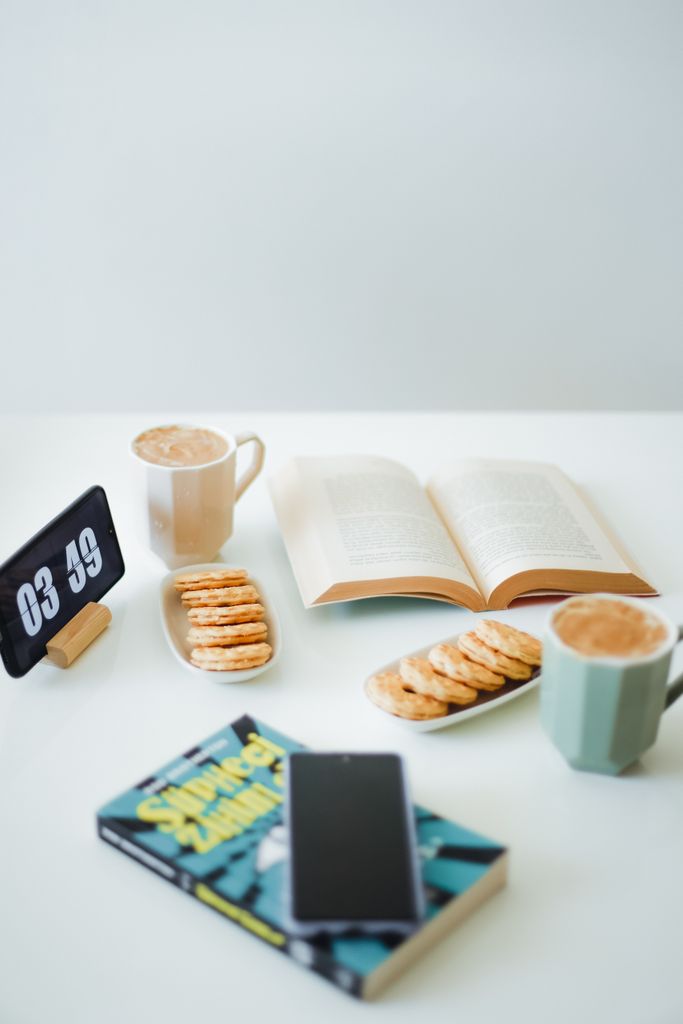 A cozy tabletop scene with coffee, cookies, books, and a digital clock for a relaxed setting.