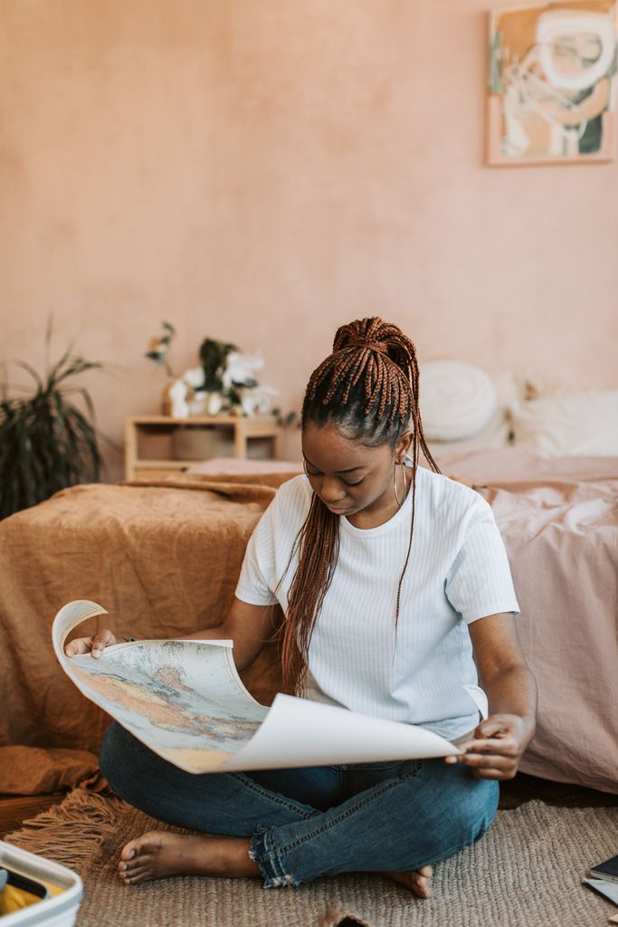 A young woman with braided hair examines a map indoors, symbolizing travel planning for an armchair global staycation 