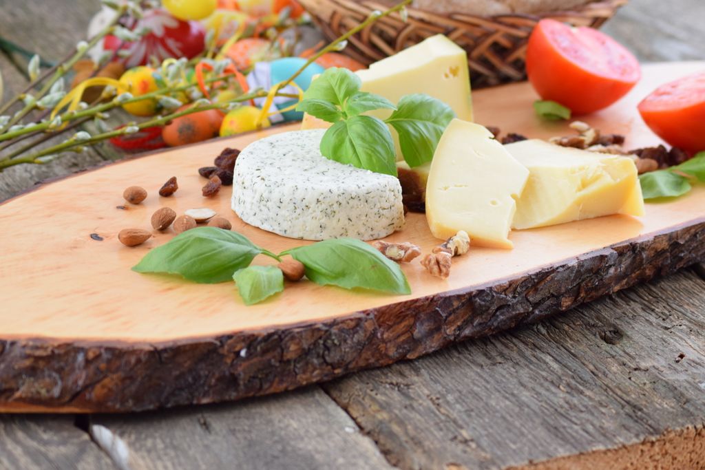 Artisan cheese slices with fresh basil and nuts on a wooden grazing table board.