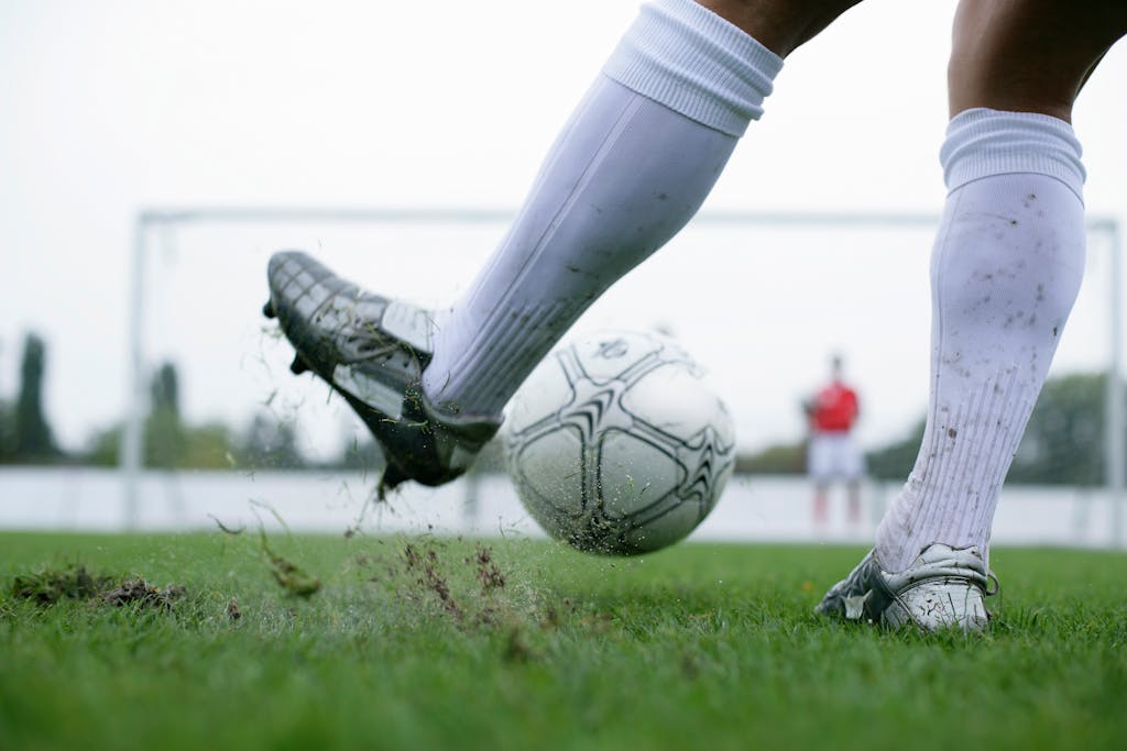 Close-up of a football player kicking a ball with motion and intensity on a grass field, showcasing action and sport.