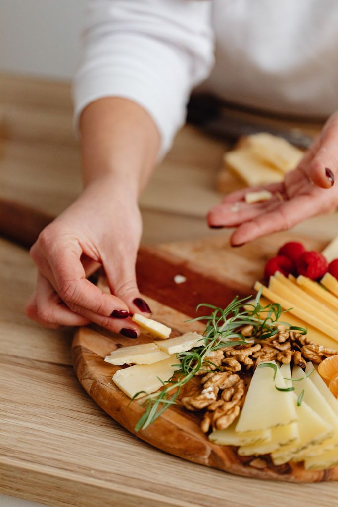 Close-up of hands arranging a cheese and nut charcuterie on Wooden boards arranged for a gorgeous grazing table on a budget