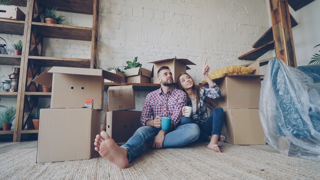 Couple relaxing with coffee among moving boxes, planning new home.