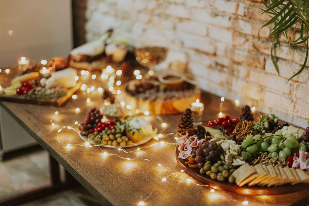 Cozy indoor scene of a beautifully arranged cheese and fruit platter with festive candles and lights.
