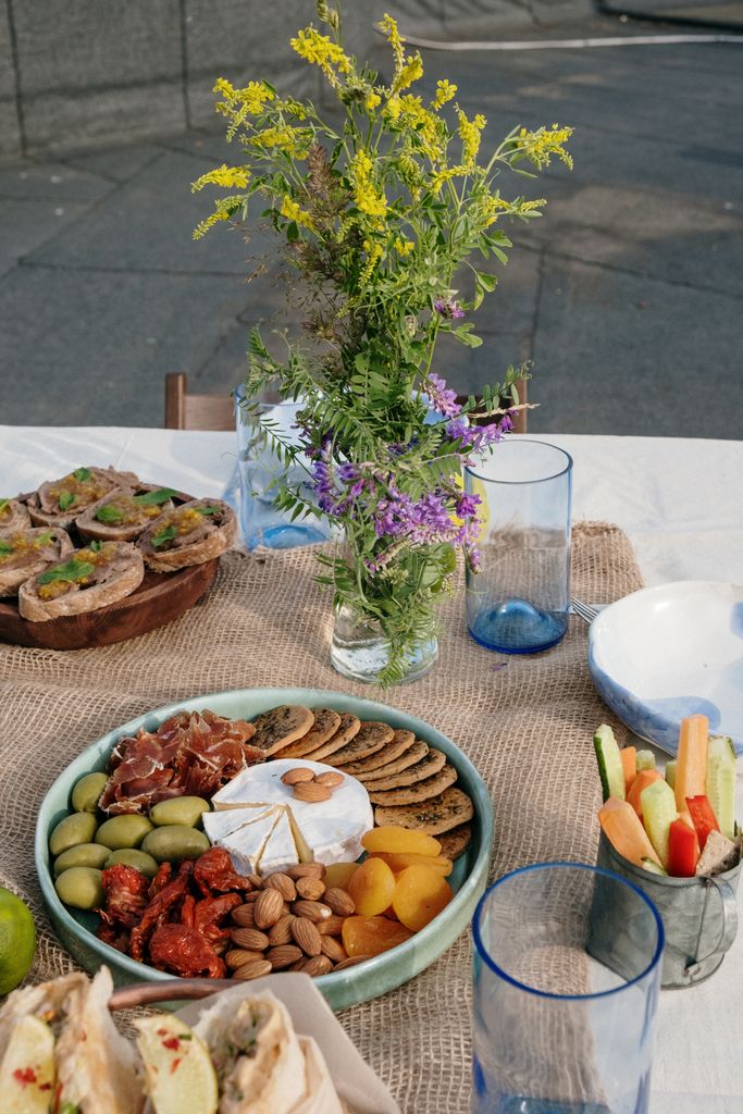 Enjoy an outdoor Gorgeous Grazing table featuring a cheese platter with fresh veggies, crackers, and flowers on a sunny day.