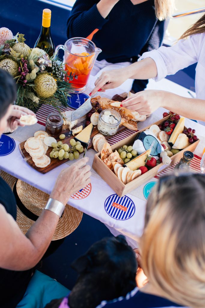 From above of crop faceless people eating cheese and fruits and drinking lemonade and wine while having summer grazing party
