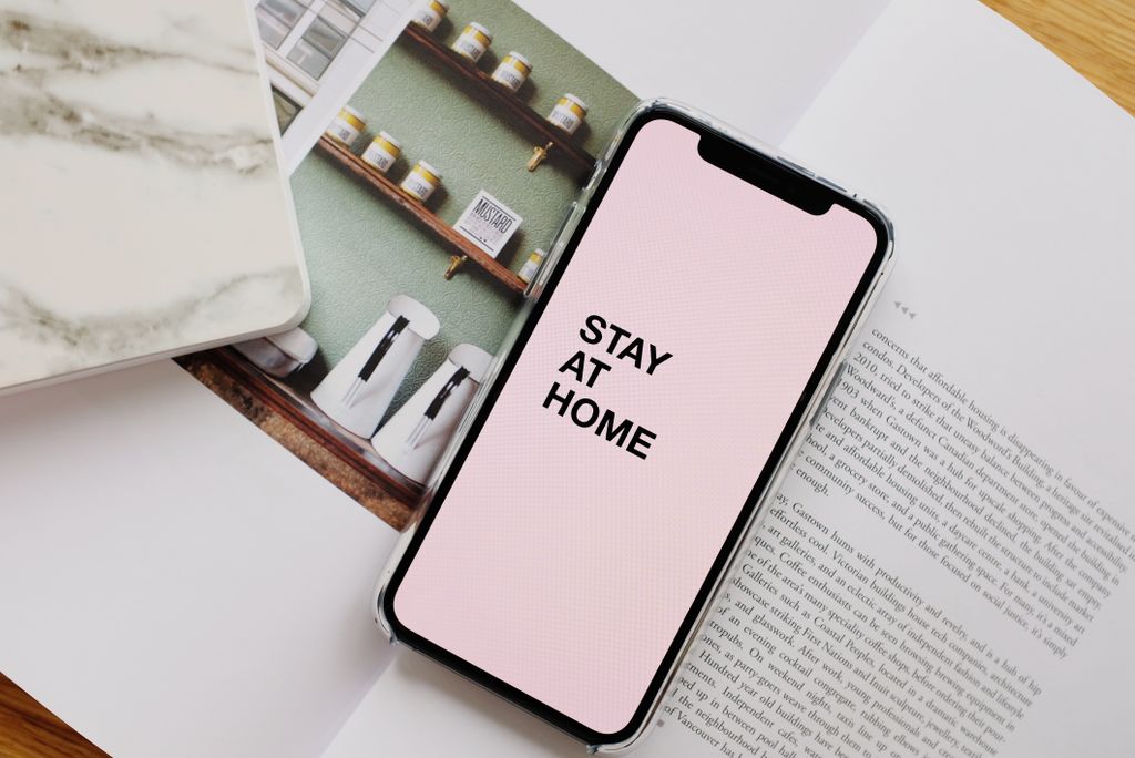 From above of modern cellphone with pale pink screen and STAY AT HOME inscription put on open magazine for a peaceful reading retreat at home corner