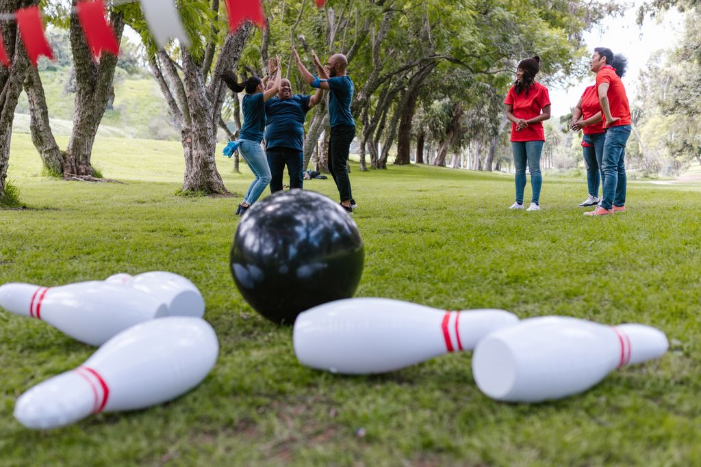 Group of adults enjoying an outdoor team-building activity with inflatable bowling pins in a park.