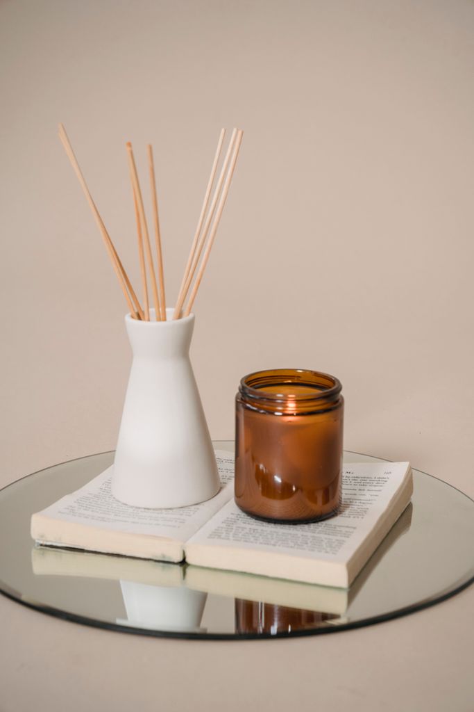 Minimalist still life of an amber jar and incense holder on an open book with a mirror base.