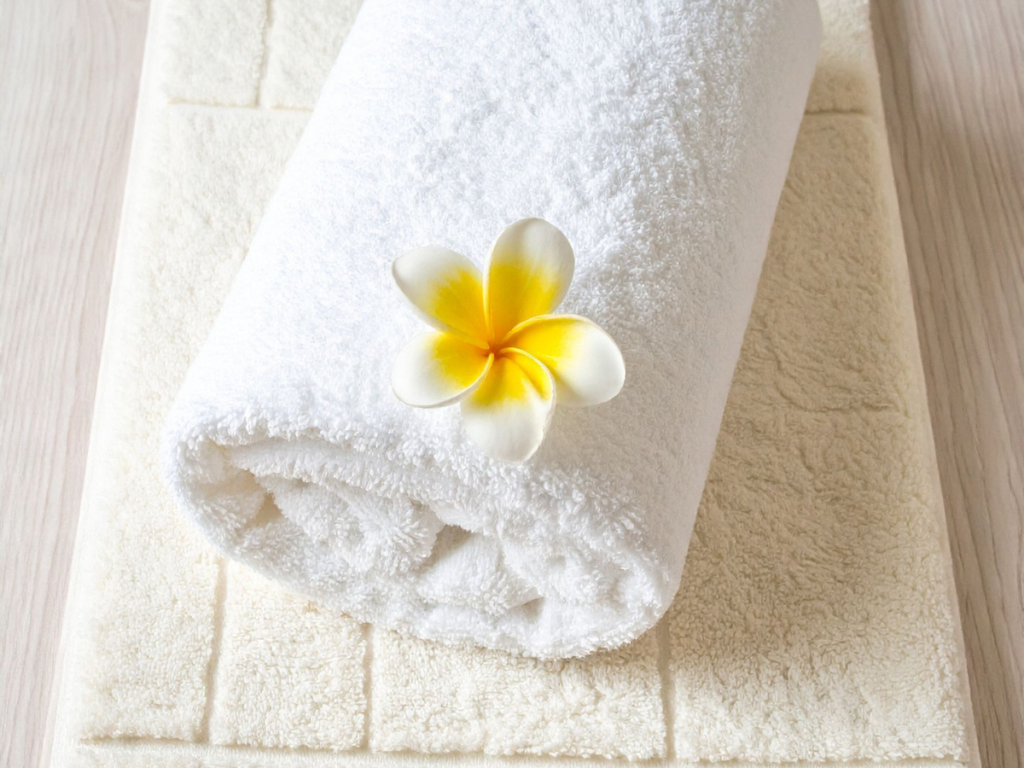 Luxury Bath mat with rolled white towel and yellow flower placed on top