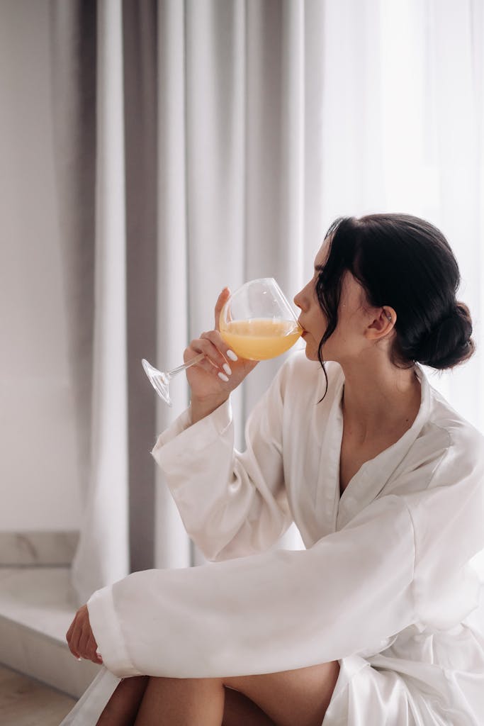 Woman in a white bathrobe enjoying a glass of orange juice indoors as part of a summer unwind routine