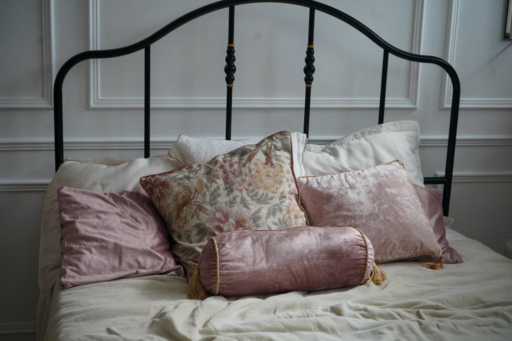 A slim elegant black metal frame headboard behind bed decorated with pink cushions.