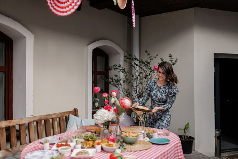 A woman prepares an outdoor table for a festive gathering with flowers and food.